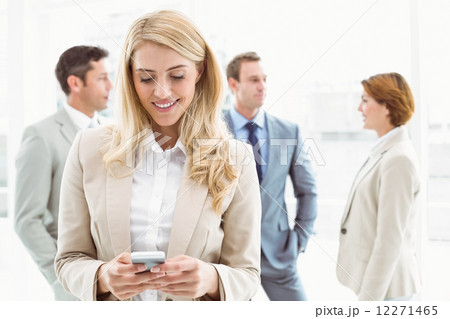 Businesswoman text messaging with colleagues in meeting behind Businesswoman text messaging with colleagues in meeting behind 12271465