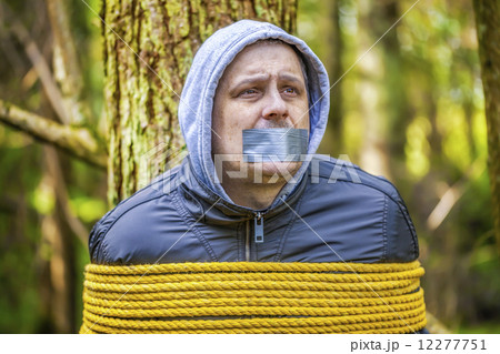 Man with tape on mouth tied to the tree in the forest  12277751
