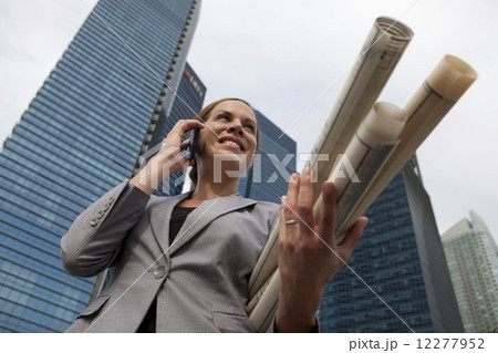 Businesswoman holding architectural plans talking on phone outdoors  12277952