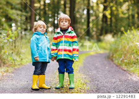 Two little sibling boys in colorful raincoats and boots walking Two little sibling boys in colorful raincoats and boots walking 12291483