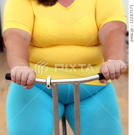 overweight woman exercising on bike simulator 12297573