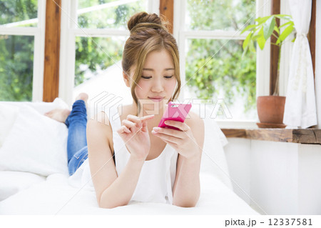 寝転んでスマホを操作する若い女性の写真素材