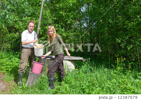 Young happy pair at a well, pours water in a bucket.. 12387079
