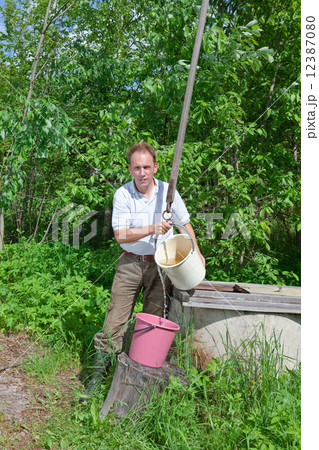 man at a well, pours water in a bucket 12387080