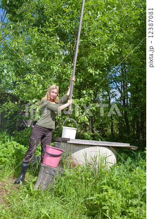 The young woman at a well, pours water in a bucket 12387081