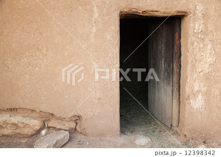 Old rural clay wall with open wooden door. Background texture 12398342