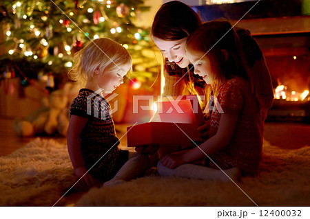 Mother and her daughters opening a Christmas gift 12400032