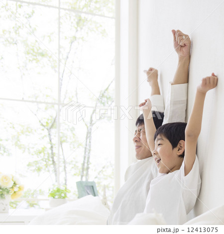 ベッドで背伸びをする親子 12413075