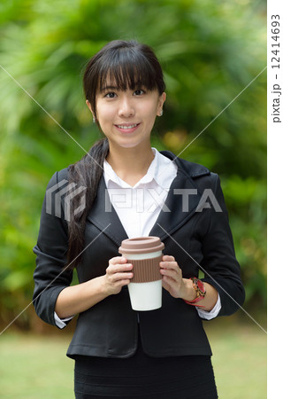 One successful young chinese business woman holding coffee mug in front of greenery 12414693
