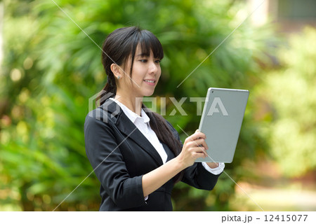 One successful young chinese business woman using mobile device tablet iPad in front of greenery 12415077
