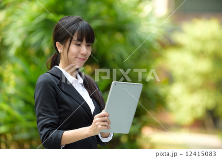 One successful young chinese business woman using mobile device tablet iPad in front of greenery 12415083