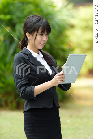 One successful young chinese business woman using mobile device tablet iPad in front of greenery 12415143