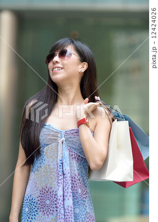 Young chinese woman shopping with sunglass shopping bags standing outside of mall along promenade 12424026