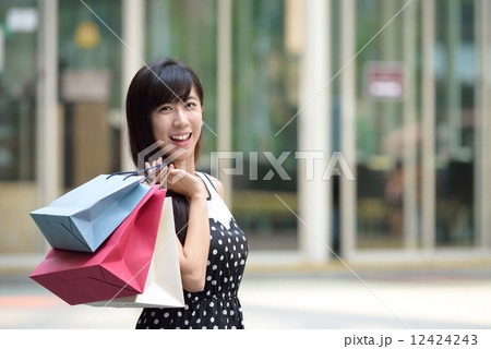 Young chinese woman shopping with shopping bags standing outside of mall along promenade 12424243