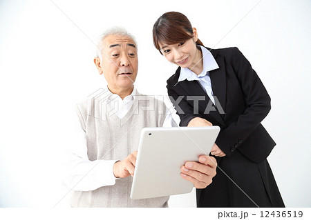 シニア男性にタブレットを使って説明するスーツの女性 12436519