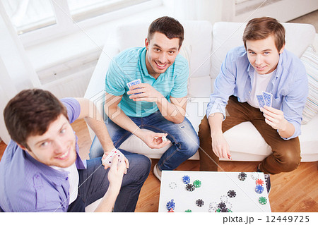 three smiling male friends playing cards at home 12449725