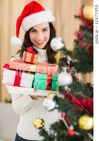 Festive brunette holding pile of gifts near a christmas tree Festive brunette holding pile of gifts near a christmas tree 12471956