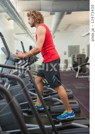 Side view of man working out on x-trainer in gym Side view of man working out on x-trainer in gym 12473430