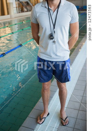 Low section of a swimming coach with stopwatch by pool 12473563