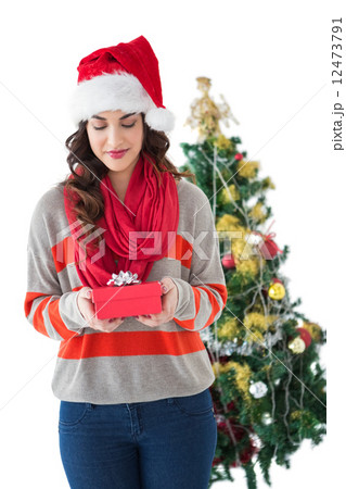 Festive brunette holding gift by the tree 12473791