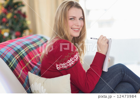 Smiling blonde writing while sitting on the sofa Smiling blonde writing while sitting on the sofa 12473984