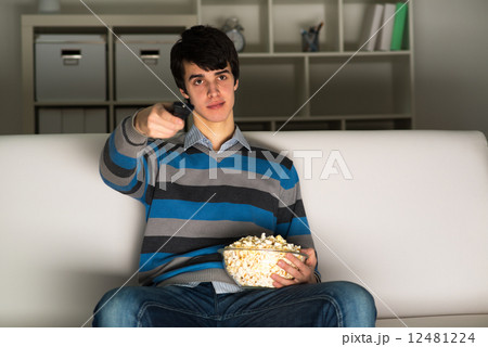 young man watching television with popcorn 12481224
