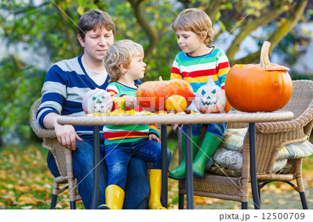 Dad and two little sons making jack-o-lantern for halloween in a 12500709