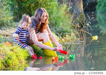 Adorable little girl and her mom playing with paper boats in a r Adorable little girl and her mom playing with paper boats in a r 12500906