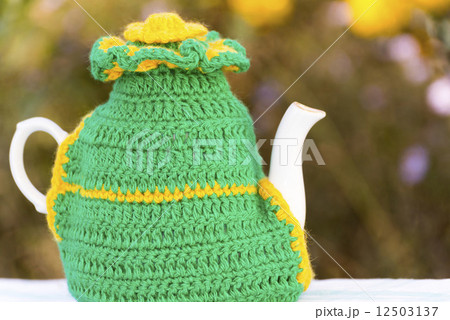 Knitted doily on the teapot on a natural background. 12503137