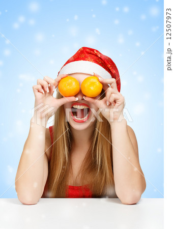Woman in santa claus hat joking with mandarins Woman in santa claus hat joking with mandarins 12507973
