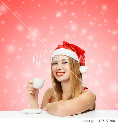 Beautiful young woman in santa claus hat siting at the table wit 12507980