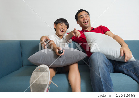 An Asian father and son having a good laugh watching TV comedy program in the living room 12512468