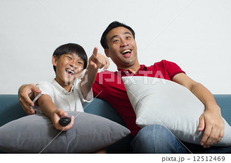 An Asian father and son having a good laugh watching TV comedy program in the living room 12512469