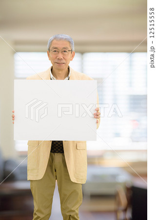 リビングルームにホワイトボードを持って立っているシニア男性 12515558