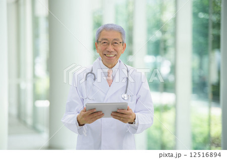 大病院のエントランスにタブレットを持って立っているロマンスグレーの医師 12516894