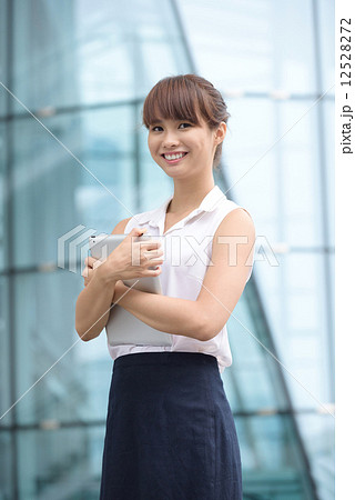 Young successful Chinese business woman using mobile device tablet iPad in front of office building 12528272
