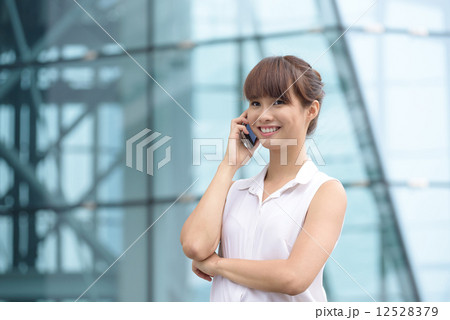 Young successful Chinese business woman making voice call in front of glass office building 12528379