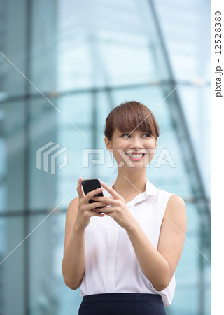 Young successful Chinese business woman using smart phone in front of glass office building 12528380