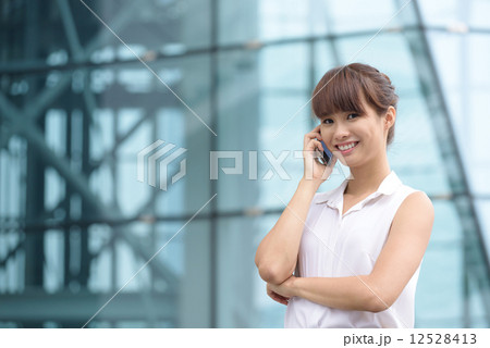 Young successful Chinese business woman making voice call in front of glass office building Young successful Chinese business woman making voice call in front of glass office building 12528413