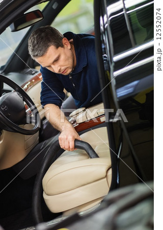Worker on a car wash cleaning car interior with vacuum cleaner 12552074