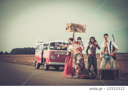 Multi-ethnic hippie hitchhikers with guitar and luggage on a road 12552322