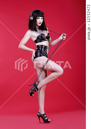 Glamor. Woman DJ in Heels and Stagy Latex Costume with Headphones 12552472