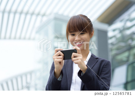 One young Chinese office lady using smart phone in front of office building 12565781