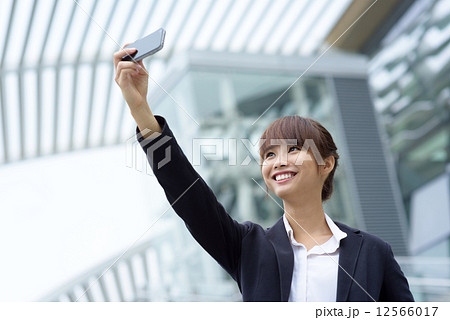 One young chinese office lady taking selfies with her smart phone in front of office building One young chinese office lady taking selfies with her smart phone in front of office building 12566017
