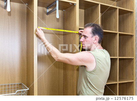 The man is engaged in assemblage of a new wardrobe The man is engaged in assemblage of a new wardrobe 12576175