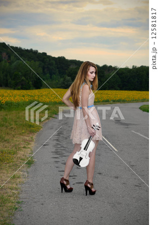 Woman stands with vilolin by country road Woman stands with vilolin by country road 12581817
