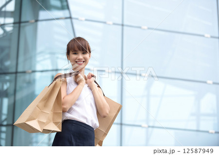 One young Asian Chinese office lady with shopping bags outside of glass building 12587949