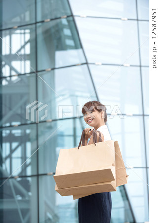 One young Asian Chinese office lady with shopping bags outside of glass building 12587951