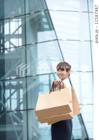 One young chinese shopaholic with her shopping buys in front of glass building mall 12587987