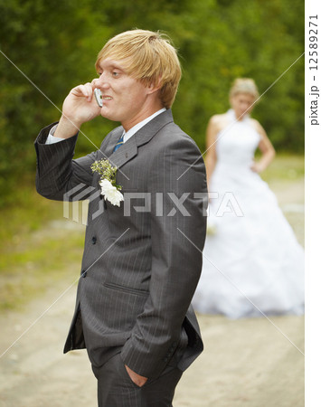 Groom has turned away from bride and speaks on phone Groom has turned away from bride and speaks on phone 12589271